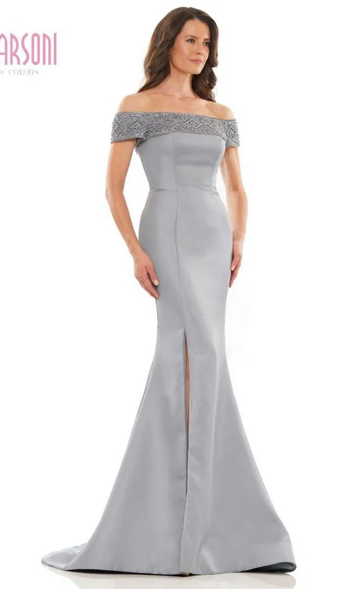 A woman models the Marsoni MV1184 Long Formal Dress featuring an off-shoulder neckline with silver beads, a mermaid skirt and front slit, set against a plain white background.